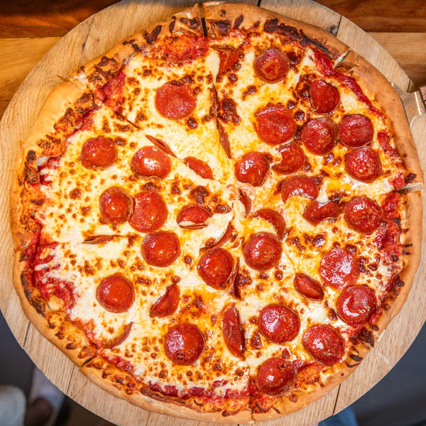 A whole pepperoni pizza with melted cheese and tomato sauce on a wooden serving board.