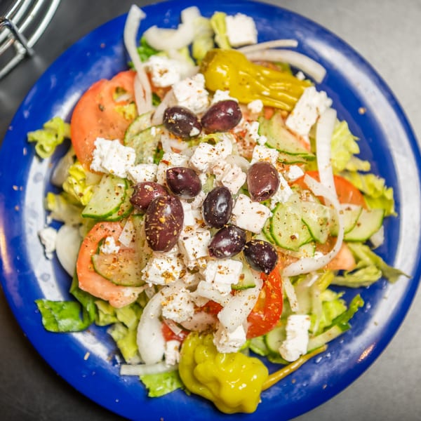 A vibrant Greek salad with lettuce, tomatoes, cucumbers, onions, feta, olives, and a pepperoncini.