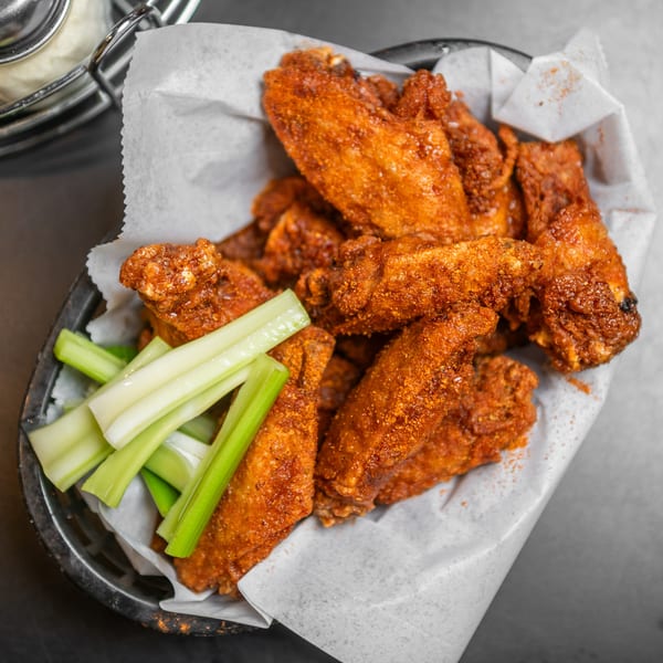 A basket of crispy, seasoned chicken wings with celery sticks, served on a dark table.