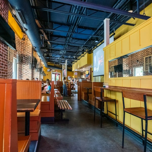 A casual restaurant interior with orange booths, brick walls, yellow accents, and a large projection screen.