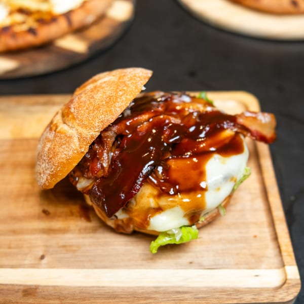 Gourmet burger with melted cheese, bacon, and barbecue sauce on a wooden board.