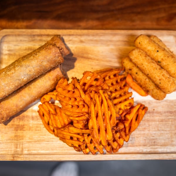 Crispy egg rolls, waffle fries, and mozzarella sticks arranged on a wooden serving tray.