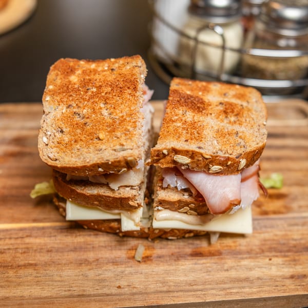 Toasted ham and cheese sandwich on whole grain bread, cut in half on a wooden board.
