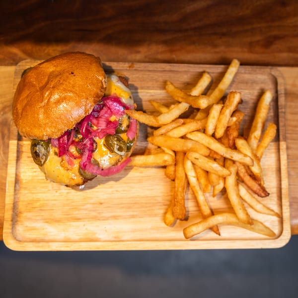 A cheeseburger with pickled onions and jalapeños, served with french fries on a wooden tray.