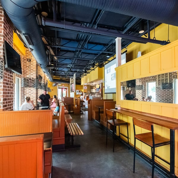Restaurant interior with brick walls, yellow accents, orange booths, and people dining.