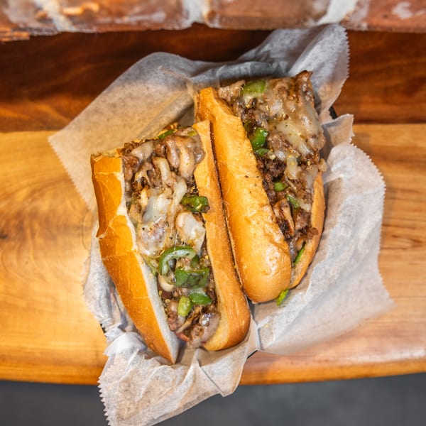 Two halves of a cheesy steak and pepper sub sandwich on a wooden table.